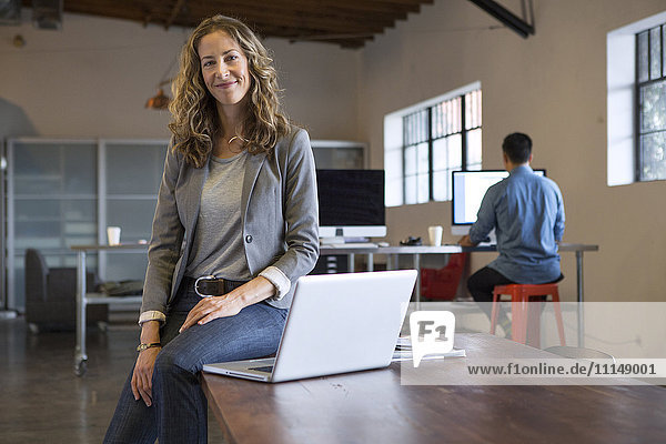 Businesswoman sitting on desk with laptop
