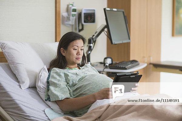 Schwangere Chinesin im Krankenhauszimmer mit digitalem Tablet
