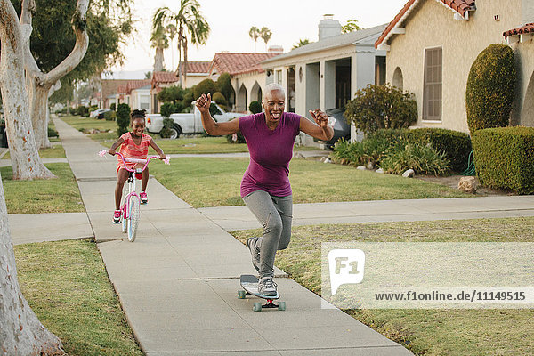 Mutter und Tochter fahren Skateboard und Fahrrad auf dem Bürgersteig