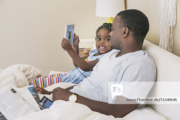 African American father and daughter using digital tablet on bed