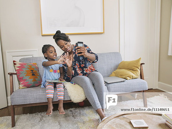 Afroamerikanische Mutter und Tochter machen ein Selfie im Wohnzimmer