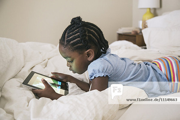 African American girl using digital tablet on bed