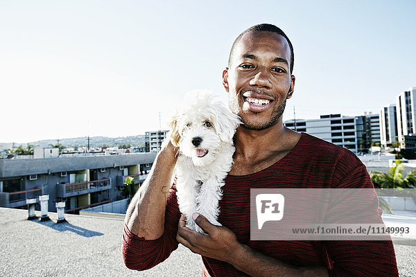 Afroamerikanischer Mann hält Hund auf städtischem Dach