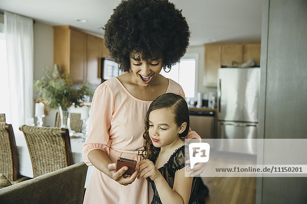 Gemischtrassige Mutter und Tochter benutzen ein Mobiltelefon