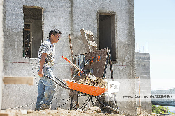 Hispanischer Bauarbeiter schiebt Schubkarre auf der Baustelle