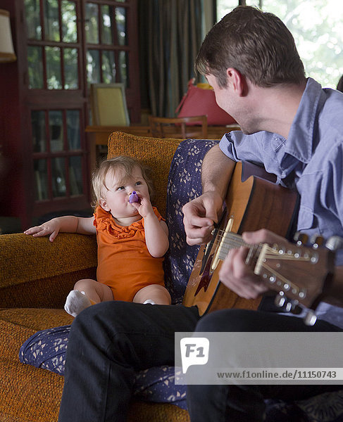 Caucasian father playing guitar for daughter