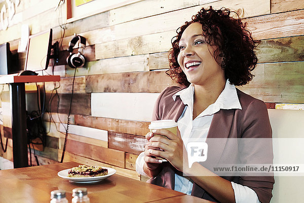 Mixed race businesswoman having coffee and pastry in cafe
