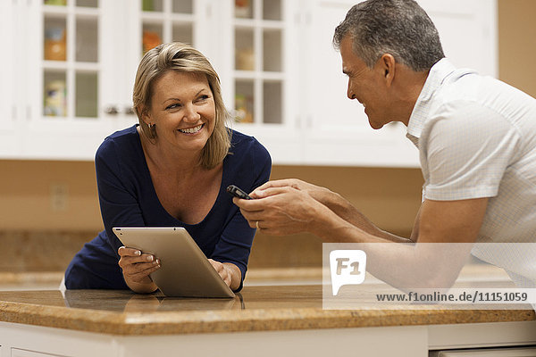 Caucasian couple using digital tablet and cell phone at kitchen counter