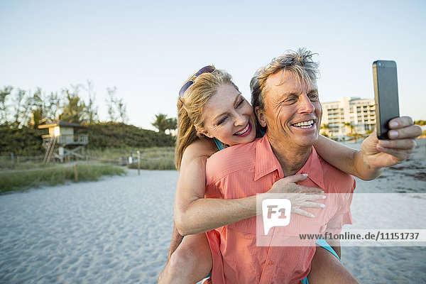 Older Caucasian couple taking cell phone selfie on beach