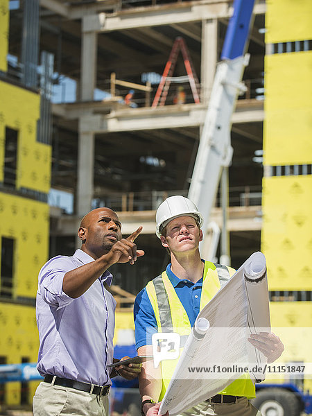Geschäftsmann und Bauarbeiter lesen Baupläne auf der Baustelle