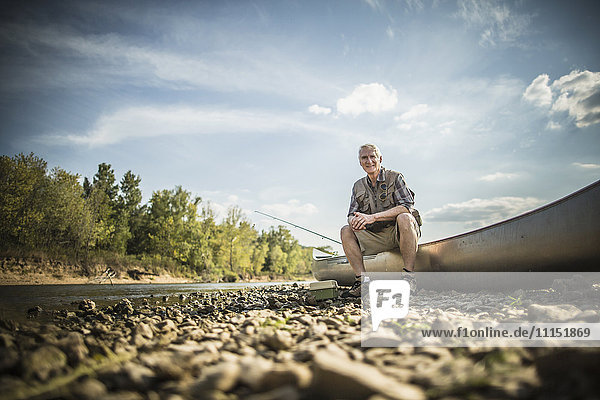 Älterer kaukasischer Mann sitzt im Kanu auf dem Flussbett