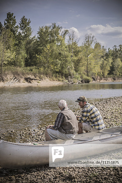 Kaukasischer Vater und Sohn sitzen im Kanu auf dem Flussbett