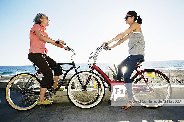 Caucasian mother and daughter riding bicycles near beach