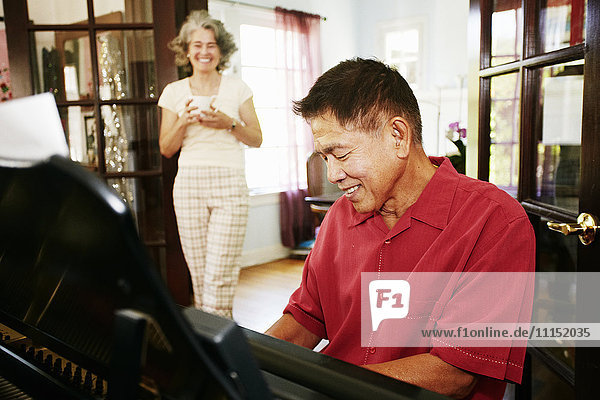 Woman watching husband playing piano in living room