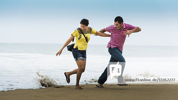 Hispanisches Paar spielt in der Nähe von Wellen am Strand
