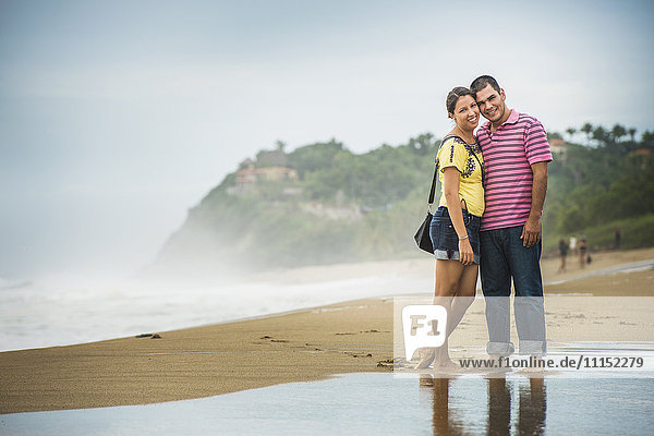 Hispanic couple hugging in waves on beach