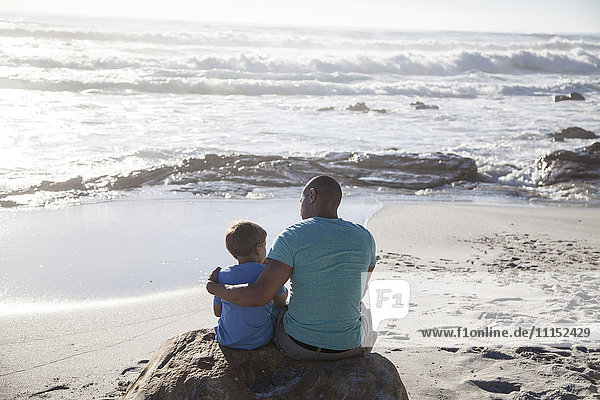 Mixed race father and son sitting on beach