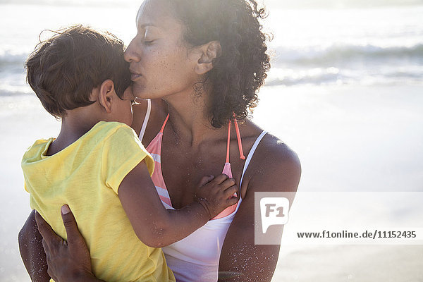 Gemischtrassige Mutter küsst Tochter am Strand