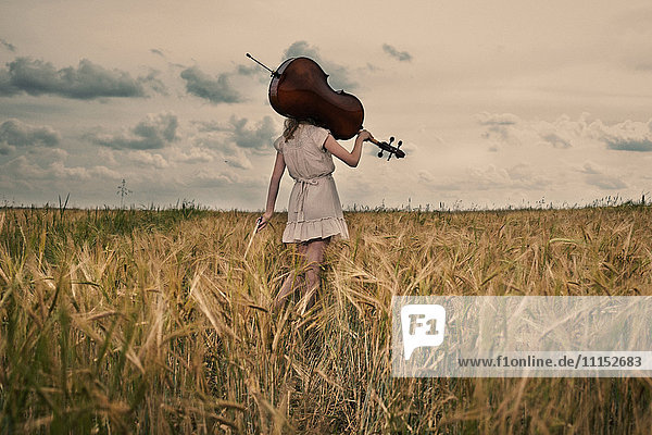 Caucasian girl carrying cello on shoulder in rural fieldCaption