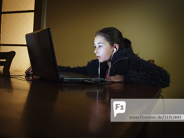 Gemischtrassiges Mädchen  das am Abend am Tisch einen Laptop benutzt