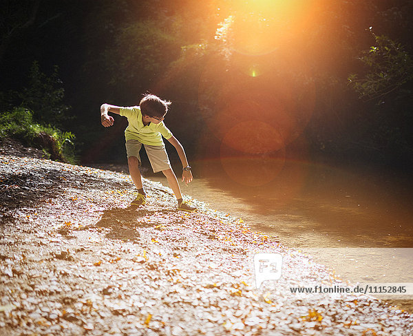 Mixed race boy skipping stones in stream