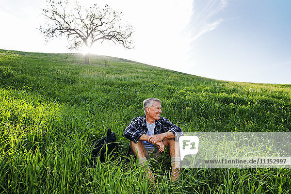 Älterer kaukasischer Mann sitzt auf einem grasbewachsenen Hügel