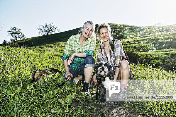 Kaukasische Mutter und Tochter gehen mit ihren Hunden auf einem grasbewachsenen Hügel spazieren