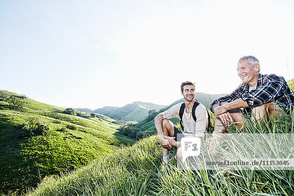 Caucasian father and son sitting on grassy hillside