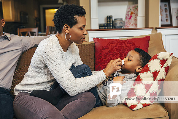 Schwarze Frau wischt die Nase ihres Sohnes auf dem Sofa ab