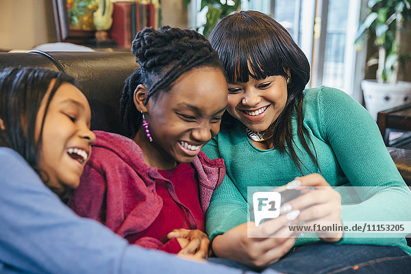 Schwarze Schwestern benutzen Handy auf Sofa