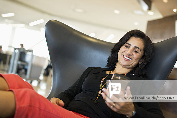 Hispanische Geschäftsfrau benutzt Mobiltelefon im Flughafen