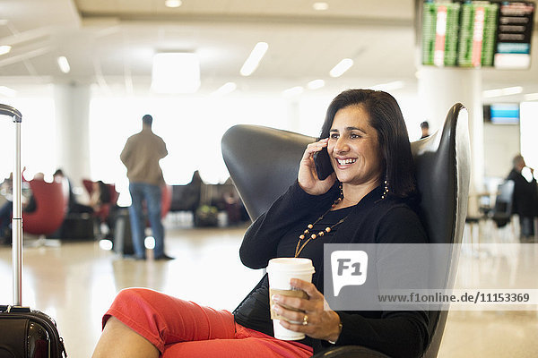Hispanische Geschäftsfrau  die im Wartebereich eines Flughafens mit ihrem Handy telefoniert