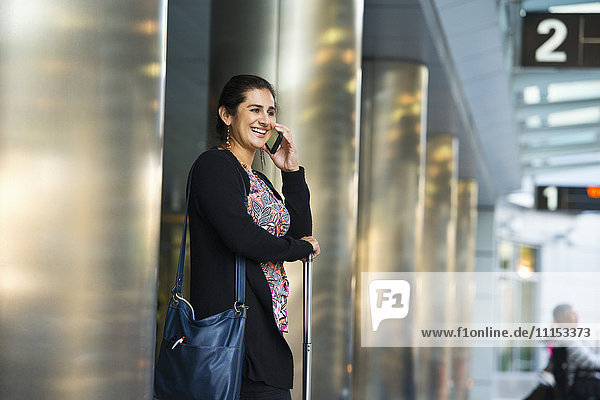Hispanische Geschäftsfrau  die im Flughafen mit einem Handy telefoniert