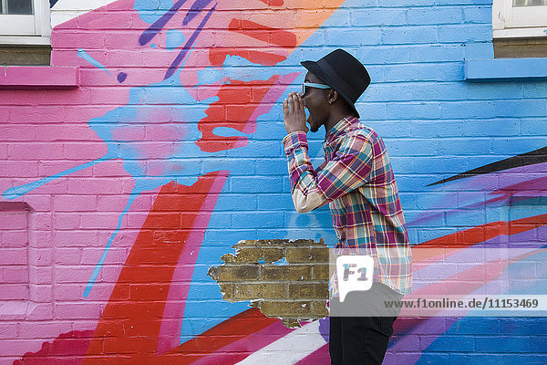 Black man in sunglasses shouting near colorful wall