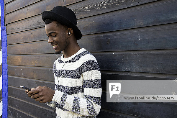 Black man listening to mp3 player near wooden wall