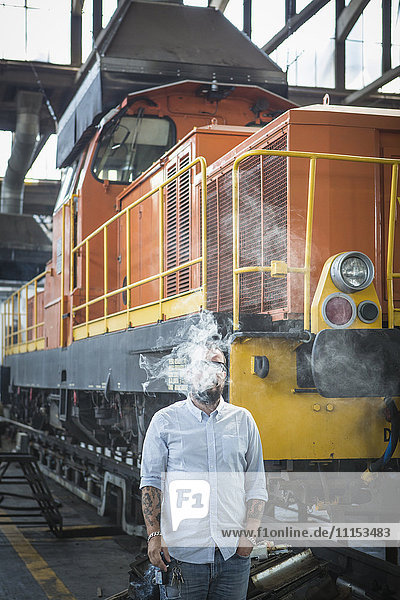 Caucasian man blowing smoke in train yard