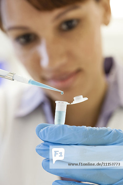 Gemischtrassige Wissenschaftlerin  die im Labor eine Probe in ein Reagenzglas pipettiert