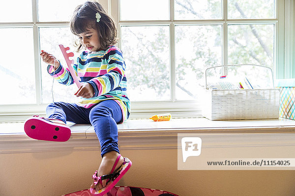Mädchen spielt mit Spielzeug auf der Fensterbank