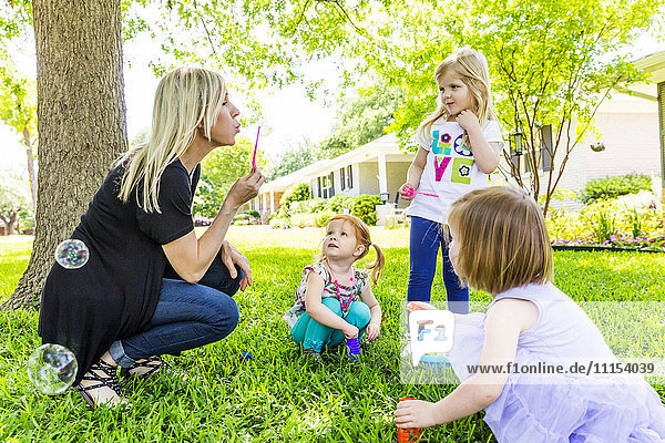 Caucasian mother and daughters blowing bubbles in backyard