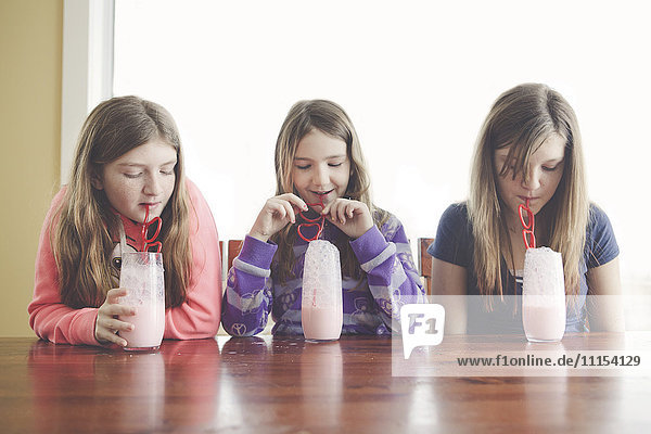 Kaukasische Mädchen trinken Milch mit gekräuselten Strohhalmen am Tisch