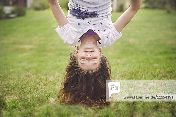 Caucasian girl hanging upside down in backyard
