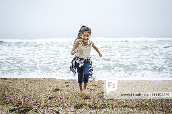 Hispanisches Mädchen läuft barfuß am Strand