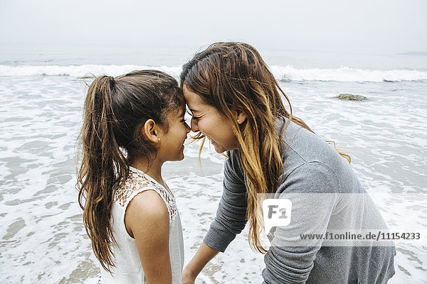 Hispanische Mutter und Tochter stehen am Strand