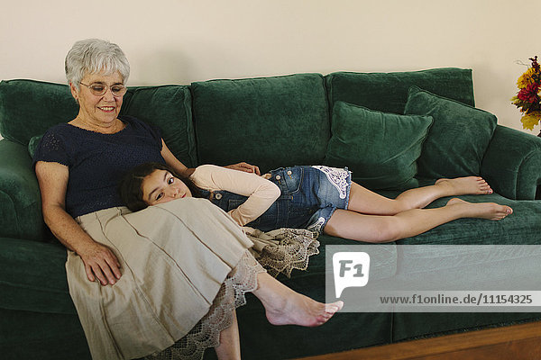 Grandmother and granddaughter sitting on sofa in living room