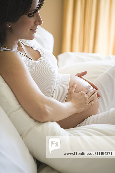 Schwangere Frau reibt ihren Bauch auf dem Sofa
