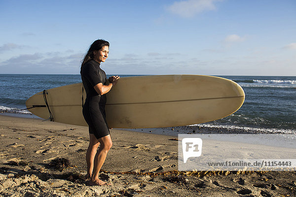 Hispanic surfer carrying surfboard on beach