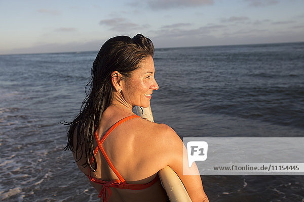 Hispanische Frau hält Surfbrett im Meer