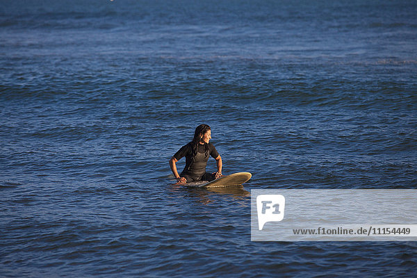 Hispanischer Surfer schwimmt auf Surfbrett im Meer