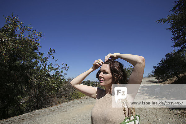 Kaukasische Frau  die ihr Haar auf einem Feldweg feststeckt
