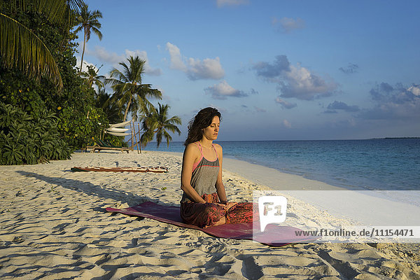 Kaukasische Frau meditiert am tropischen Strand
